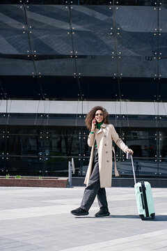 Young african woman walking outdoors carrying a suitcase and going to travel by airplane at modern airport. Vacations, travel and active lifestyle concept     