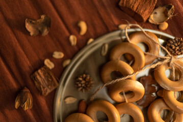 A bunch of bagels lie on a bronze platter, decorated with dried flowers and herbs. On a background of brown corrugated paper