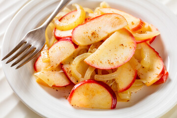 fried onion and red apple slices on white plate with fork on white wood table, close-up