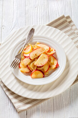 fried onion and red apple slices on white plate with fork on white wood table, vertical view from above