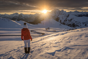 woman in red jacket watching sunset over curvy road in the alps, passo Giau