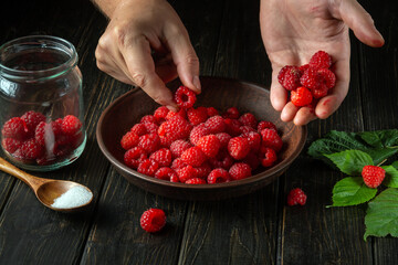 The chef is sorting through fresh red raspberries in the kitchen to prepare a sweet soft drink. Cooking diet desserts