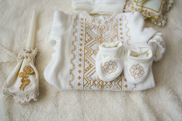 clothes for the baptism of a newborn baby and a candle with an angel on a light background