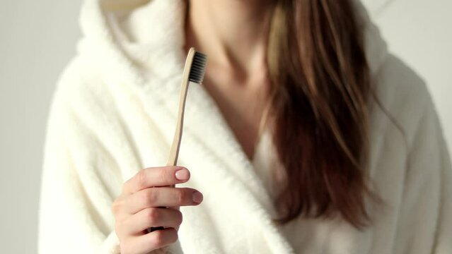 Hand holding bamboo toothbrush. Ecological biodegradable, no plastic. A woman in a beige bathrobe.