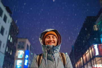 Fototapeta na wymiar snowfall woman in a blue jacket and yellow hat christmas outside, city portrait in snowfall, young model posing in Dusseldorf city, fabulous advent evening