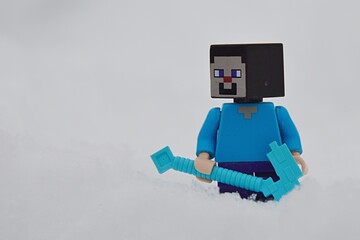 Fototapeta premium LEGO Minecraft smiling figure of Steve standing with his diamond pickaxe in deep snow.