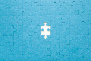 Unfinished blue puzzle without last one piece on white table background. Closeup. Top down view.