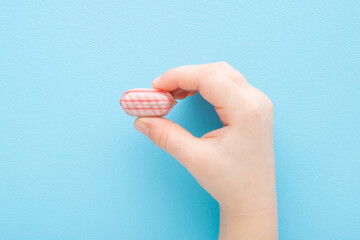 Little child fingers holding colorful sugar candy on light blue table background. Pastel color. Sweet snack. Closeup. Top down view.