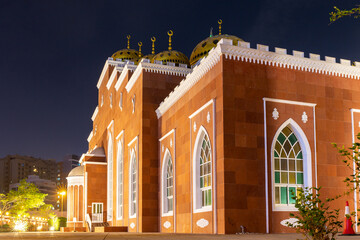 Al Salam Mosque (Masjid) in Al Barsha, Dubai, mosque with red facade and golden ornaments at night with stained glass windows.