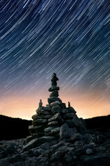 Night sky with star trails over stacked balanced stone arrangement, centered vertical composition