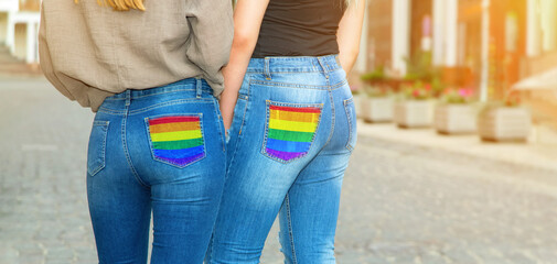 Two women in jeans with an lgbt symbol on their pocket. View from the back, no faces visible.