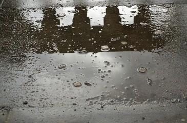 Wasserpfütze auf grauem Steinboden mit Wasserblasen und Spiegelung von altem Betongeländer bei Regen am Nachmittag im Winter