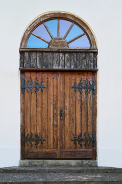 Old wooden door with arched window in the white wall of the church