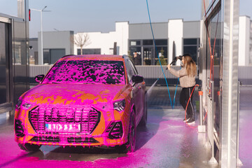 Young woman cleaning her car with a jet sprayer. Self-service car washing. Orange auto