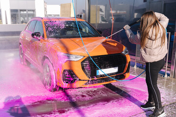 Young woman cleaning her car with a jet sprayer. Self-service car washing. Orange auto
