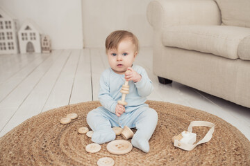 little cute baby in blue overalls plays with wooden toys sitting on a wicker carpet at home, environmentally friendly toys and the concept of motherhood and environmental care