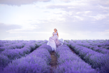 beautiful woman in a lush long dress runs in a lavender field. A girl in the image of a fairy and a princess of flowers.