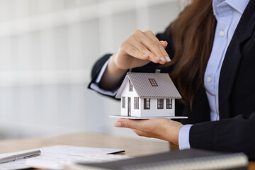 Wooden toy house with real estate agent Asian business woman signs a purchase contract mortgagefor...