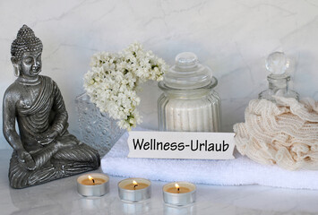 Buddha mit Kerzen, Handtuch und dem Text Wellness-Urlaub
