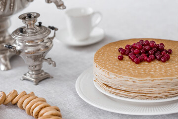 Russian traditions. Russian holiday Maslenitsa. Still life with a cup of tea, a stack of pancakes with northern cranberries, cubes of butter and samovars on the table.