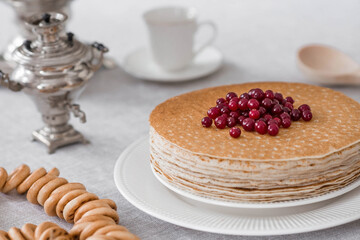 Russian traditions. Russian holiday Maslenitsa. Still life with a cup of tea, a stack of pancakes with northern cranberries, cubes of butter and samovars on the table.