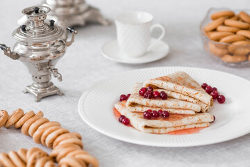 Russian traditions. Russian holiday Maslenitsa. Still life with a cup of tea, a stack of pancakes with northern cranberries, cubes of butter and samovars on the table.