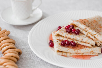 Russian traditions. Russian holiday Maslenitsa. Still life with a cup of tea, a stack of pancakes with northern cranberries, cubes of butter on the table.