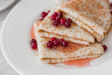 Russian traditions. Russian holiday Maslenitsa. Still life with a cup of tea, a stack of pancakes with northern cranberries, cubes of butter on the table.