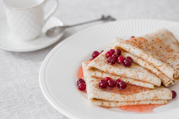 Russian traditions. Russian holiday Maslenitsa. Still life with a cup of tea, a stack of pancakes with northern cranberries, cubes of butter on the table.