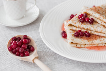Russian traditions. Russian holiday Maslenitsa. Still life with a cup of tea, a stack of pancakes with northern cranberries, cubes of butter on the table.