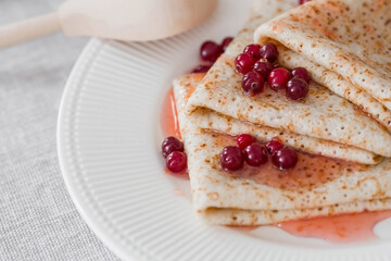 Russian traditions. Russian holiday Maslenitsa. Still life with a cup of tea, a stack of pancakes with northern cranberries, cubes of butter on the table.