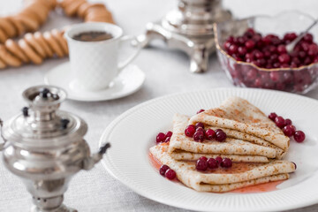 Russian traditions. Russian holiday Maslenitsa. Still life with a cup of tea, a stack of pancakes with northern cranberries, cubes of butter and samovars on the table.