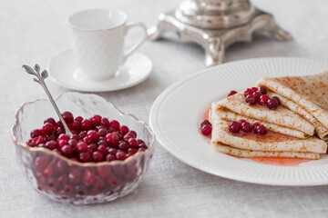 Russian traditions. Russian holiday Maslenitsa. Still life with a cup of tea, a stack of pancakes with northern cranberries, cubes of butter and samovars on the table.