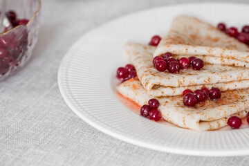 Russian traditions. Russian holiday Maslenitsa. Still life with a cup of tea, a stack of pancakes with northern cranberries, cubes of butter on the table.