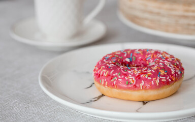 Delicious dessert. Pink donut with multicolored sprinkles, a cup of black coffee or tea. Sweets.