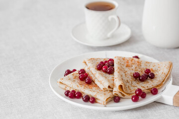 Russian traditions. Russian holiday Maslenitsa. Still life with a cup of tea, a stack of pancakes with northern cranberries, cubes of butter on the table.