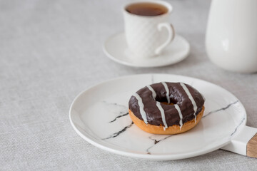 Delicious dessert. A chocolate donut with white stripes of glazes, a cup of black coffee or tea. Sweets.