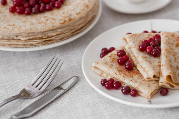 Russian traditions. Russian holiday Maslenitsa. Still life with a cup of tea, a stack of pancakes with northern cranberries, cubes of butter on the table.