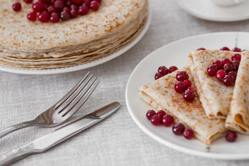 Russian traditions. Russian holiday Maslenitsa. Still life with a cup of tea, a stack of pancakes with northern cranberries, cubes of butter on the table.