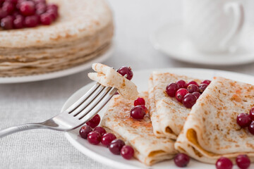 Russian traditions. Russian holiday Maslenitsa. Still life with a cup of tea, a stack of pancakes with northern cranberries, cubes of butter on the table.
