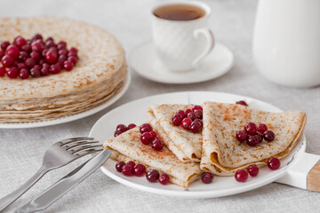 Russian traditions. Russian holiday Maslenitsa. Still life with a cup of tea, a stack of pancakes with northern cranberries, cubes of butter on the table.