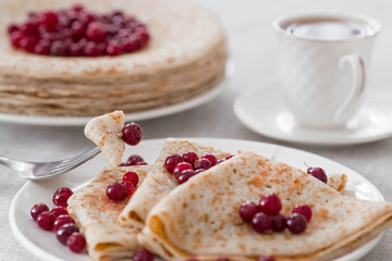 Russian traditions. Russian holiday Maslenitsa. Still life with a cup of tea, a stack of pancakes with northern cranberries, cubes of butter on the table.