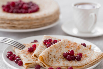 Russian traditions. Russian holiday Maslenitsa. Still life with a cup of tea, a stack of pancakes with northern cranberries, cubes of butter on the table.