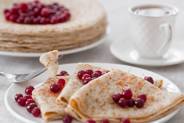 Russian traditions. Russian holiday Maslenitsa. Still life with a cup of tea, a stack of pancakes with northern cranberries, cubes of butter on the table.