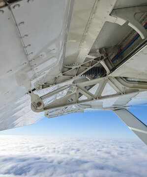 Detailed view of flaps , high-lift devices and actuators of a general aviation airplane flying at stall speed. Strut and wing of semi-cantilever high-wing aircraft over the clouds on a sunny day.