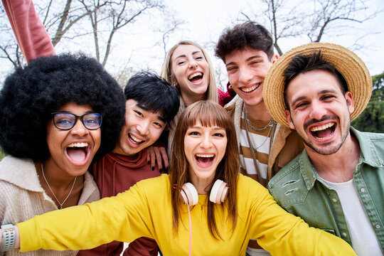 Multiracial group of happy friends taking a mobile selfie in urban park. Positive international teenagers taking a photo while strolling down the street in autumn. Big smiles and good times. 
