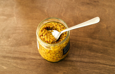 Open jar of french grainy mustard with a teaspoon inside