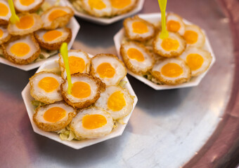 Many fried quail eggs, with cutlery inserted into white foam cups.