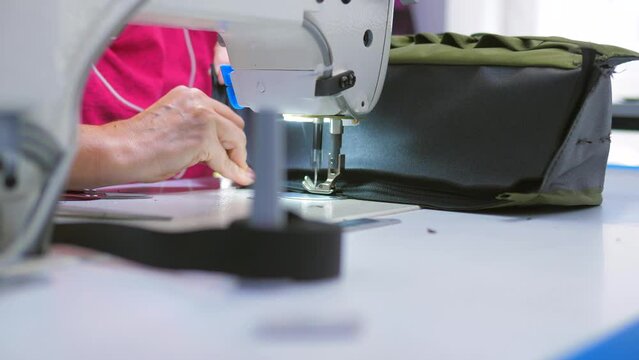 A woman wraps the straps of a backpack with a sewing machine in the production of backpacks and bags