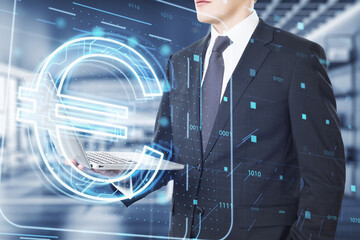 Young businessman holding tablet with glowing euro hologram on blurry office interior background. Money, digital banking and finance concept. Double exposure.